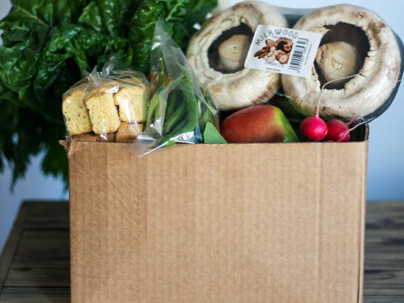 A cardboard box packed with fresh vegetables, mushrooms and groceries